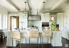 a large kitchen with white cabinets and wooden flooring, along with two bar stools