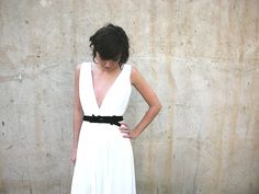 a woman standing in front of a wall with her hands on her hips wearing a white dress