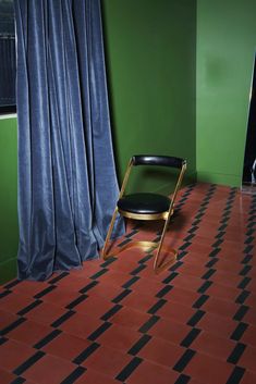 a chair sitting on top of a red tiled floor next to a window with blue curtains