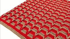 a red and beige crocheted blanket on top of a white surface