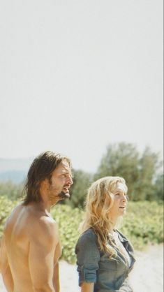 a shirtless man and woman standing next to each other on top of a sandy beach