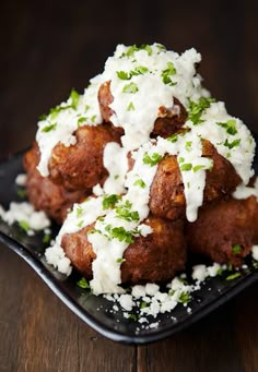 a black plate topped with fried meat covered in white sauce and parmesan cheese