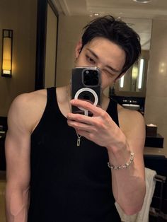 a man taking a selfie with his cell phone in a bathroom mirror, wearing a black tank top