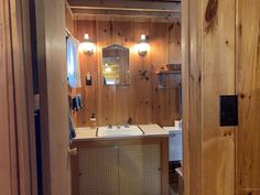 a bathroom with wood paneling and white sink under two lights on the side of the wall