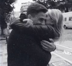 a man and woman hugging each other in front of a street with cars behind them