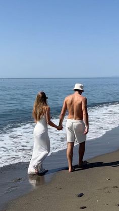 a man and woman walking on the beach holding hands