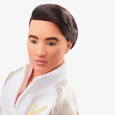 a close up of a doll wearing a white jacket and gold sequins on it's head