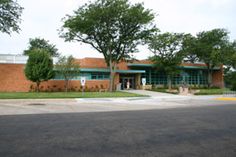 an empty parking lot in front of a building with trees on the side of it