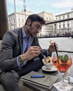 a man sitting at a table eating food with a drink in front of him on the other side