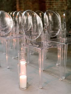 a row of clear chairs sitting next to each other with a lit candle in between them