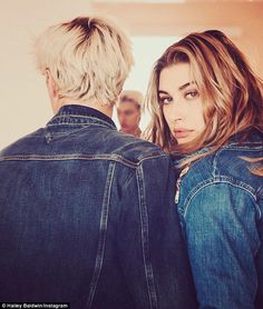 a woman with blonde hair wearing a jean jacket and looking into the distance while standing next to a man