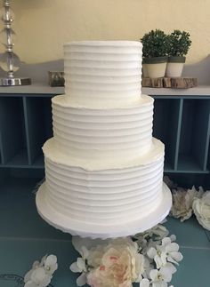 a three tiered white cake sitting on top of a blue table next to flowers