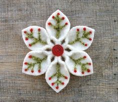 a white flower with red berries and green leaves on it's center sits on a wooden surface