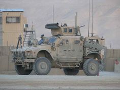 an army vehicle parked in front of a building with mountains in the backgroud