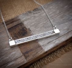 a silver bar necklace sitting on top of a wooden table