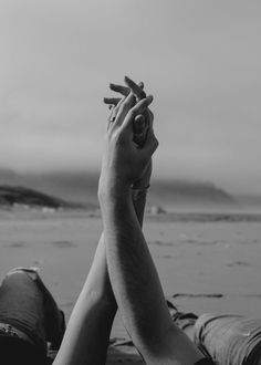 black and white photograph of two people holding their hands up to each other on the beach