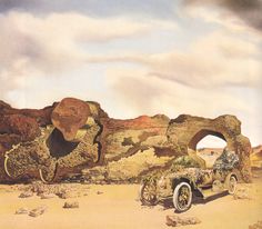 an old car is parked in front of some rocks and boulders on the desert floor