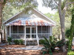 a small white house with a rusted metal roof and front porch surrounded by trees