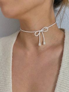 a woman wearing a white choker with a knot on the bottom and two pearls attached to it