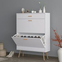 a white cabinet with shoes and vases on the floor in front of grey wall