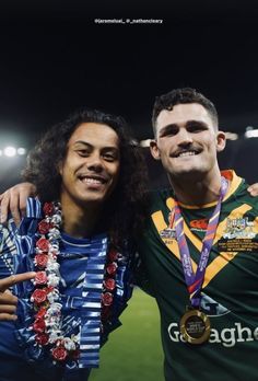 two men standing next to each other in front of a soccer field with medals around their necks