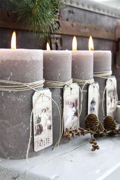 four candles with tags tied to them sitting next to pine cones and twine on a table