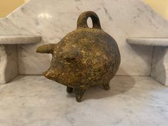 an old, rusty piggy bank sitting on top of a marble counter next to two white shelves