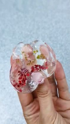 a hand holding a clear glass object with flowers in it