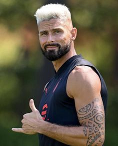 a man with white hair and tattoos giving the thumbs up sign in front of him