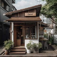 a small wooden building sitting on the side of a road next to trees and plants