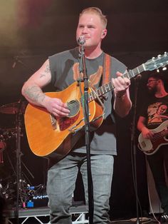 a man standing in front of a microphone while holding a guitar and singing into a microphone