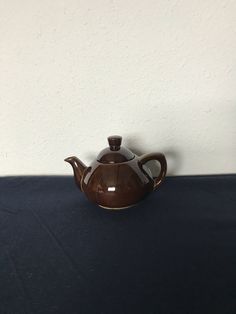 a brown tea pot sitting on top of a blue tablecloth covered table next to a white wall