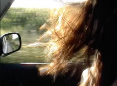 the back view of a woman's head as she drives in a car with trees and grass behind her