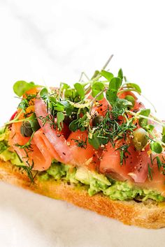 a piece of bread with avocado, salmon and sprouts on it