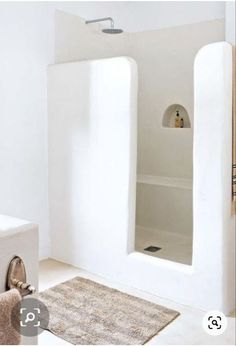 a white bathroom with an open shower stall and rug on the floor in front of it