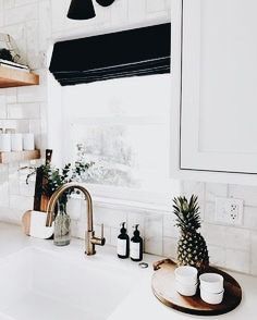 a kitchen sink sitting under a window next to a wooden tray with pineapples on it