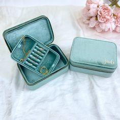 an open jewelry box sitting on top of a bed next to a pink flower bouquet