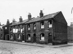 an old brick building sitting on the side of a road next to tall buildings with windows