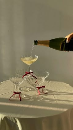 someone pouring champagne into two wine glasses on top of a white cloth covered tablecloth