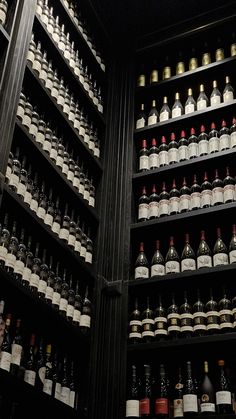 many bottles of wine are lined up on the shelves in this room with black walls