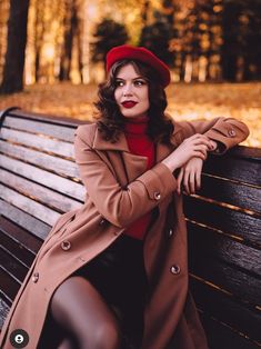 a woman sitting on top of a wooden bench wearing a red hat and trench coat