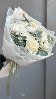 a bouquet of white flowers is held by someone's hand in front of a gray wall