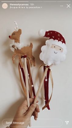 a hand holding two wooden sticks with santa and reindeer decorations on them