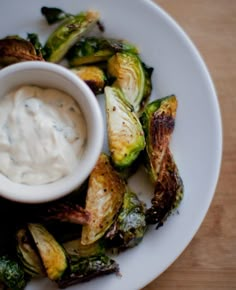 a white plate topped with roasted brussel sprouts and a small bowl of ranch dressing