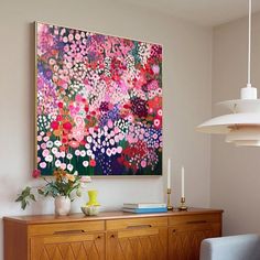 a painting is hanging on the wall next to a dresser with candles and flowers in it