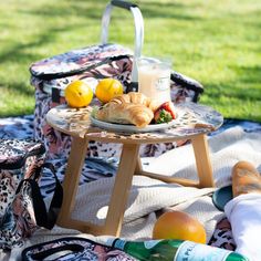 a table with food and drinks on it sitting in the grass next to a picnic blanket