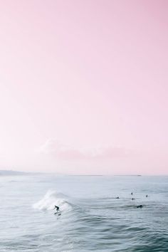 surfers are riding the waves on their surfboards in the ocean under a pink sky