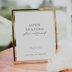 an open seating sign sitting on top of a wooden table next to a white feather