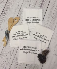 four tea towels with sayings on them sitting next to pine cones and a pair of scissors