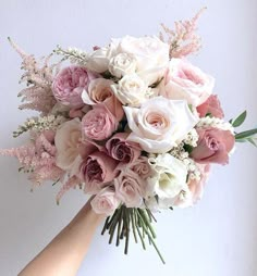 a bridal bouquet with pink and white flowers is held by a woman's hand